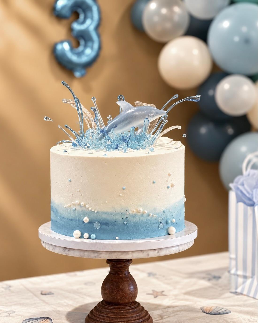 The ocean cake at the birthday party, in front of a garland of blue and white balloons and a blue number three